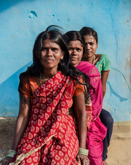 Three generations of women lined up, one behind the other on a bench. The women are wearing brightly coloured sarees.