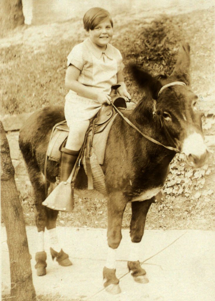 A postcard showing Janet Turnbull smiling as she sits on a donkey. A handwritten message reads in part: I am feeling fine.