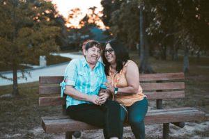 Two smiling women sitting close together on a wooden park bench.