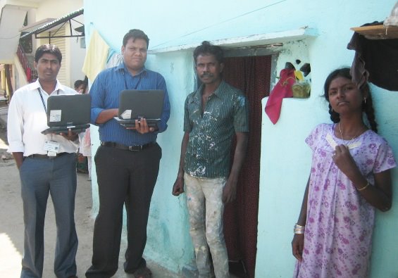 A group of researchers (two holding laptops) stand ouside of the front door of a house.