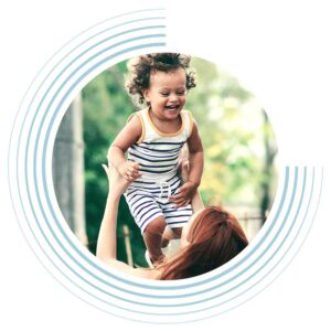 A woman with her back to the camera lifts a smiling young girl above her head.